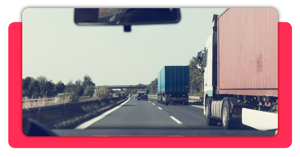 Organización del transporte y la distribución: formación gratuita 1 Dos camiones de transporte de mercancía transitan con normalidad por una carretera durante el día. A la izquierda se observa un vehículo familiar.